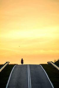 Person riding motorcycle on country road against sky during sunset