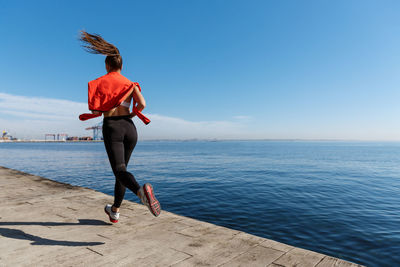 Full length of woman running by railing against sea