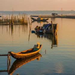 Fishing boat moored in lake against sky during sunset