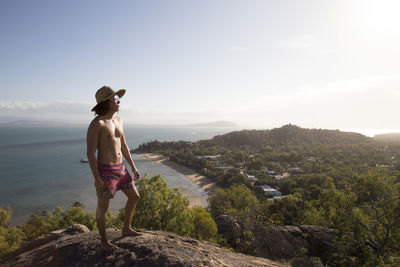 Young man with sunglasses and hat, on top of rocky hill during sunset