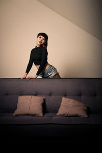 Portrait of young woman sitting on sofa against wall at home