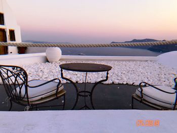 Chairs and table by swimming pool against sky during sunset