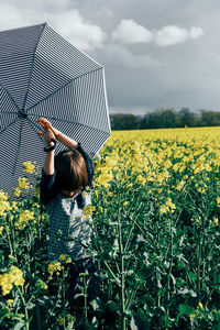 Boy holding umbrella while standing on yellow flowers field