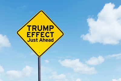 Low angle view of text on road sign against blue sky