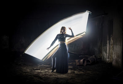 Full length of woman standing by illuminated lighting equipment in abandoned building