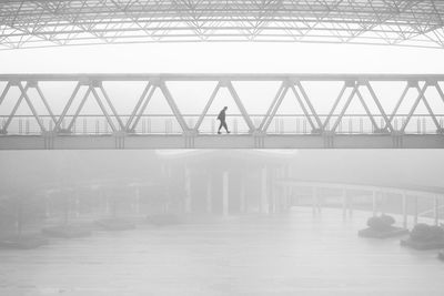Silhouette person walking on footbridge during foggy weather