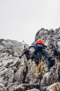 Low angle view of hiker with backpack climbing on rocky mountains against sky