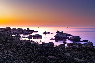 Scenic view of rocks on beach against sky during sunset