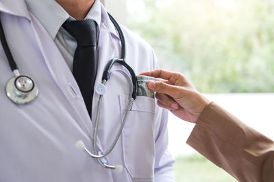 Cropped image of woman bribing doctor wearing stethoscope