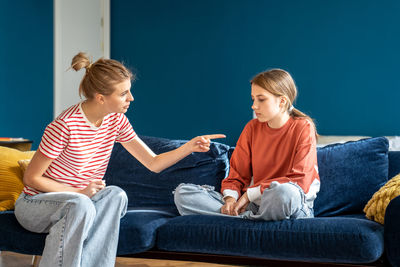 Angry mother pointing upset child sitting on sofa in living room. conflict children and parents