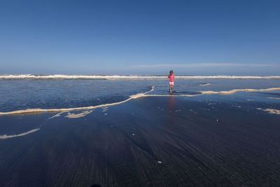 Girl walking at beach against clear blue sky