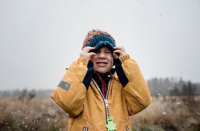 Boy covering his face with his hat whilst playing in the snow