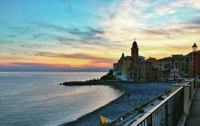 Buildings by sea against sky during sunset