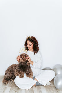 Young woman sitting with dog and balloons on floor at home