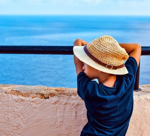 Rear view of woman wearing hat standing against sea