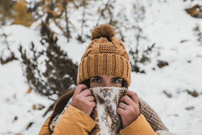 Outdoor winter portrait of young woman wearing winter clothes, holding scarf over her mouth and nose