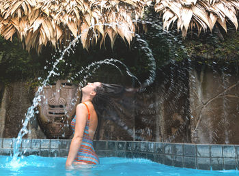 Side view of woman tossing wet hair in swimming pool