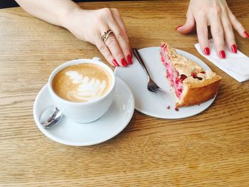 Cropped hands of woman with cake and coffee at wooden table