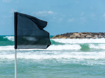 Close-up of black flag in sea against sky on sunny day