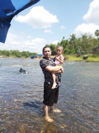 Full length portrait of happy young man in water against sky