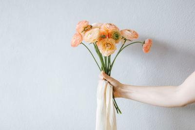 Cropped hand holding flowers against wall