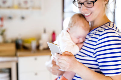 Mother holding little baby looking at cell phone