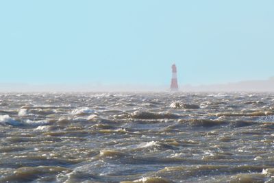 Lighthouse by sea against clear sky