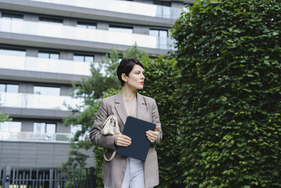 Thoughtful businesswoman with tablet pc in front of building