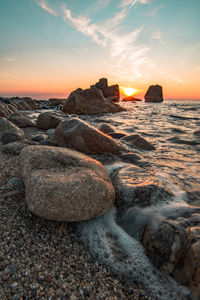 Rocks on beach against sky during sunset