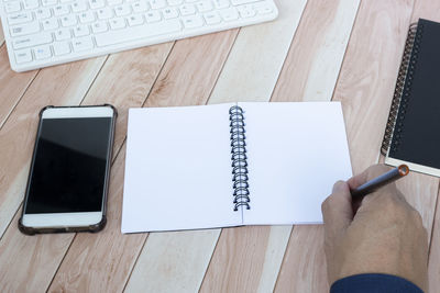 Cropped hand of man using mobile phone and book on table