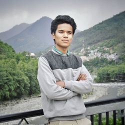 Portrait of young man standing on railing against mountain