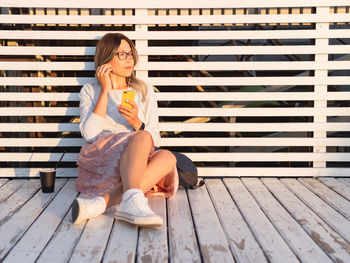 Woman with cup of coffee meets sunset on pier. female listens to music from smartphone.summer vibes.