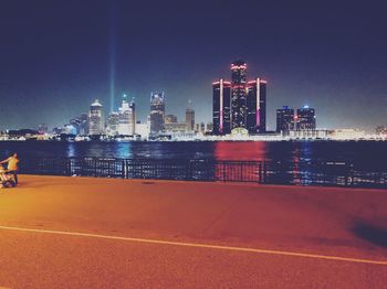 Illuminated buildings by river against sky in city at night