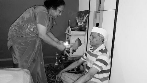 Senior woman with plate standing while male sitting by wall