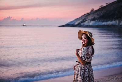 Woman standing at beach against sky during sunset