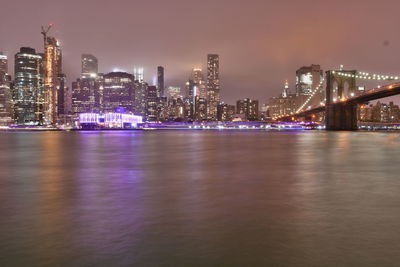 Illuminated city by river against sky at night