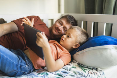 Son and father watching tablet pc lying on bed at home