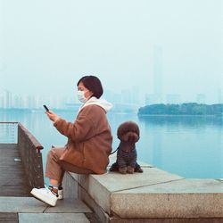 Rear view of woman sitting on mobile phone against sky