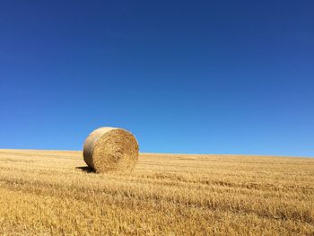 Hay bales on field against clear blue sky