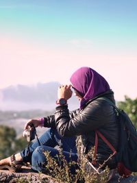 Side view of hiker sitting on mountain against sky