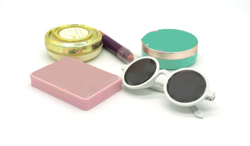High angle view of make-up products and sunglasses on white background