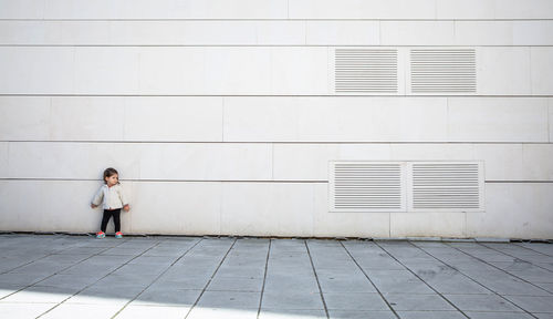 Full length of girl standing on footpath against wall in city