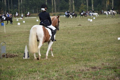 Full length rear view of jockey riding horse on grassy field