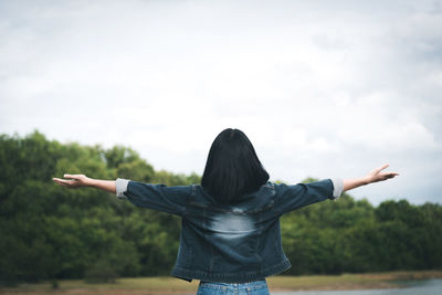 Rear view of woman with arms outstretched standing against sky