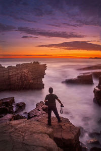 Rear view of man looking at sea against sky during sunset