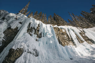 Low angle view of woman climbing on snowcapped mountain during winter