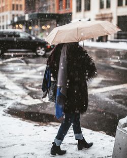 Woman walking with umbrella on street during snowfall against building