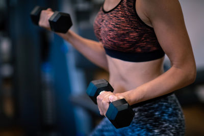 Midsection of woman lifting dumbbell in gym