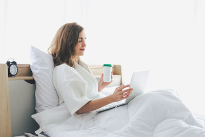 Young woman using phone while sitting on bed