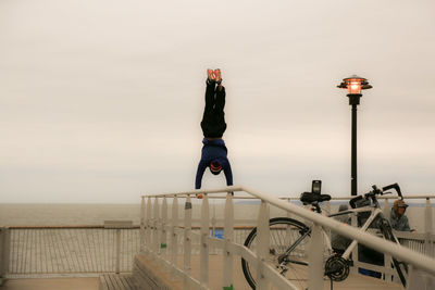 Man doing handstand on railing by sea against clear sky